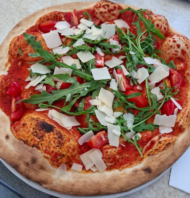 Pizza aus dem Steinofen des Capri mit Rucola, Parmesanspänen und Kirschtomaten