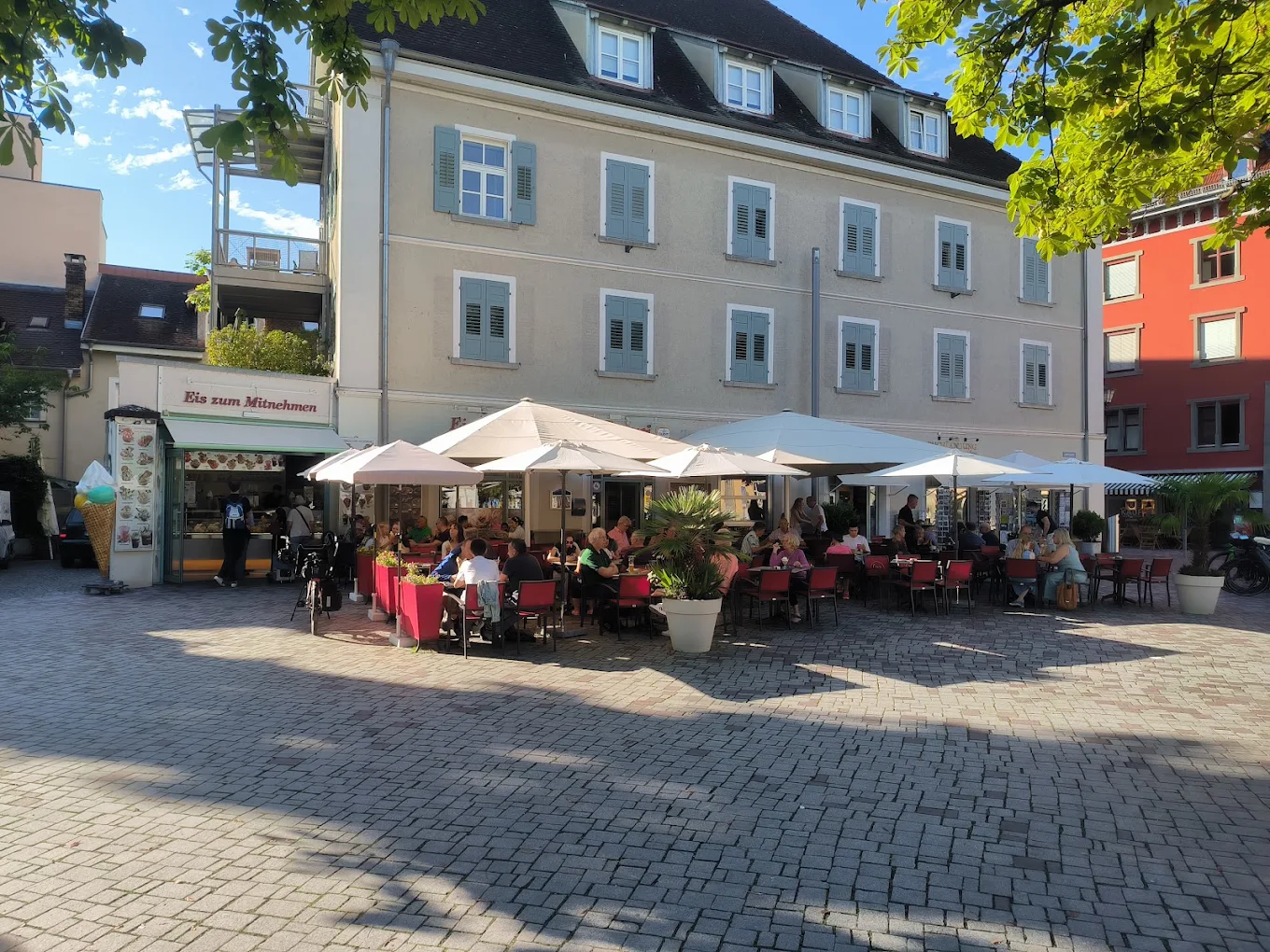 Das Capri am Landungsplatz: gut besuchte Terrasse unter Sonnenschirmen, links das Eisfenster mit Eis zum Mitnehmen